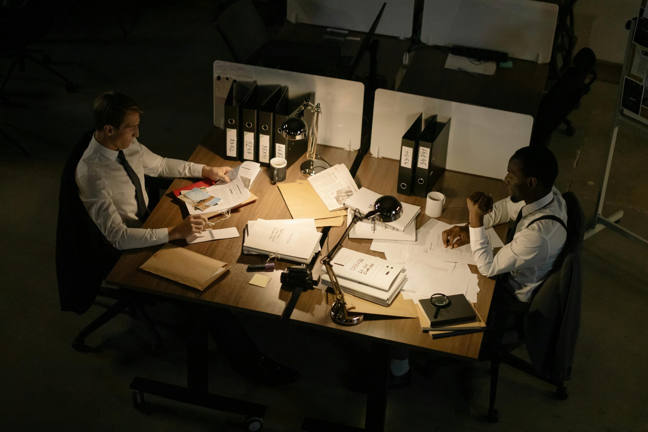 Two businessmen collaborating over documents in a dimly lit office setting.
