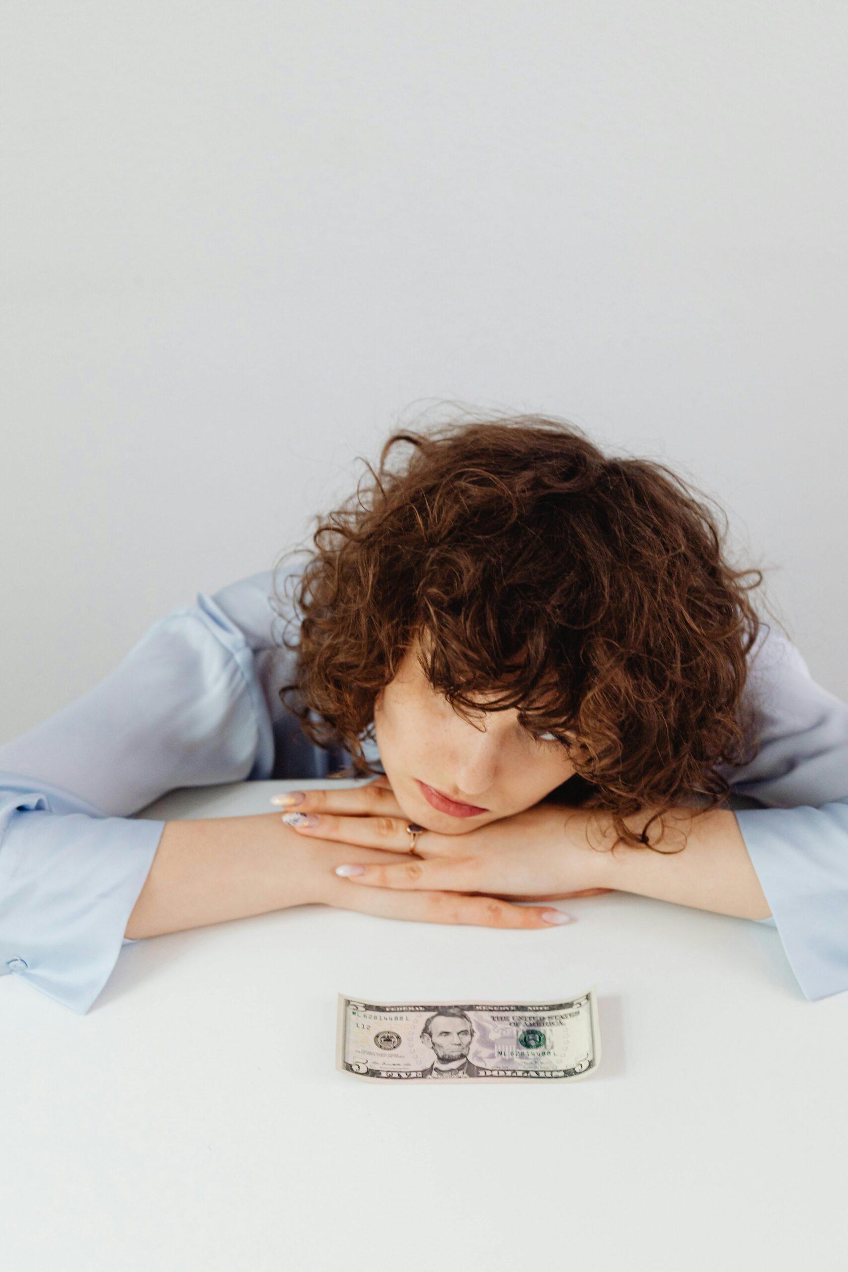 Woman with curly hair rests her head on a table gazing at money.